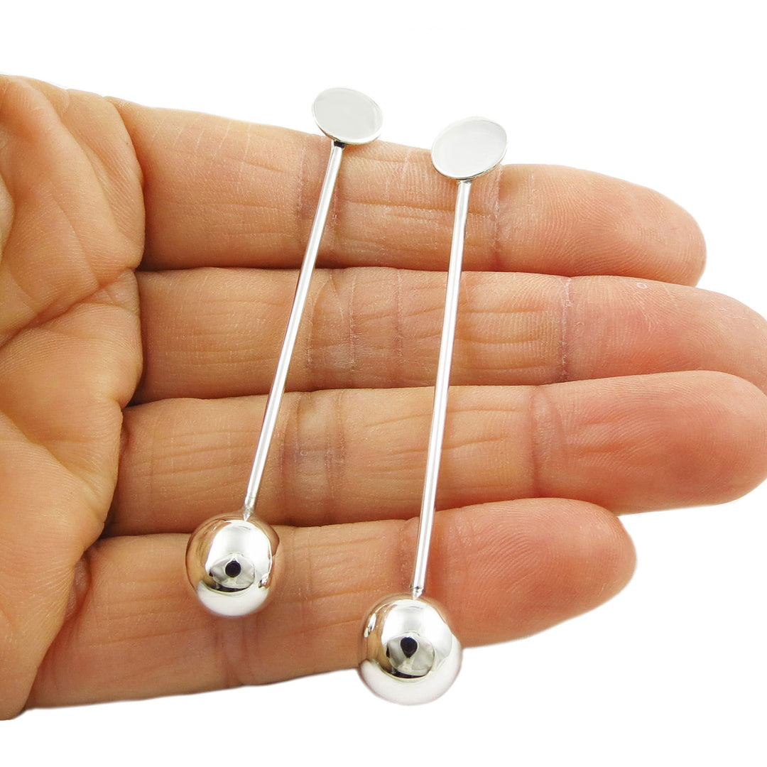 A pair of 925 sterling silver long ball bead stick earrings held in a person's hand, displaying the earrings' length and the sleek, minimalist design.