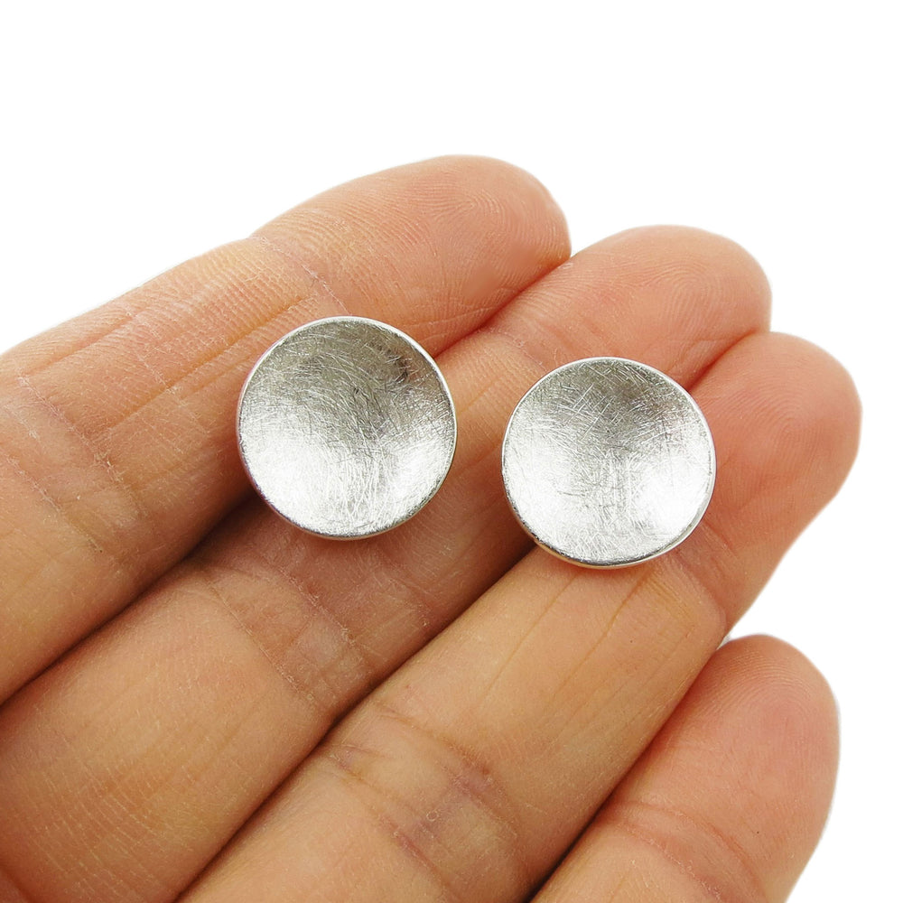 Round solid silver stud earrings with a brushed satin finish held in a person's hand.