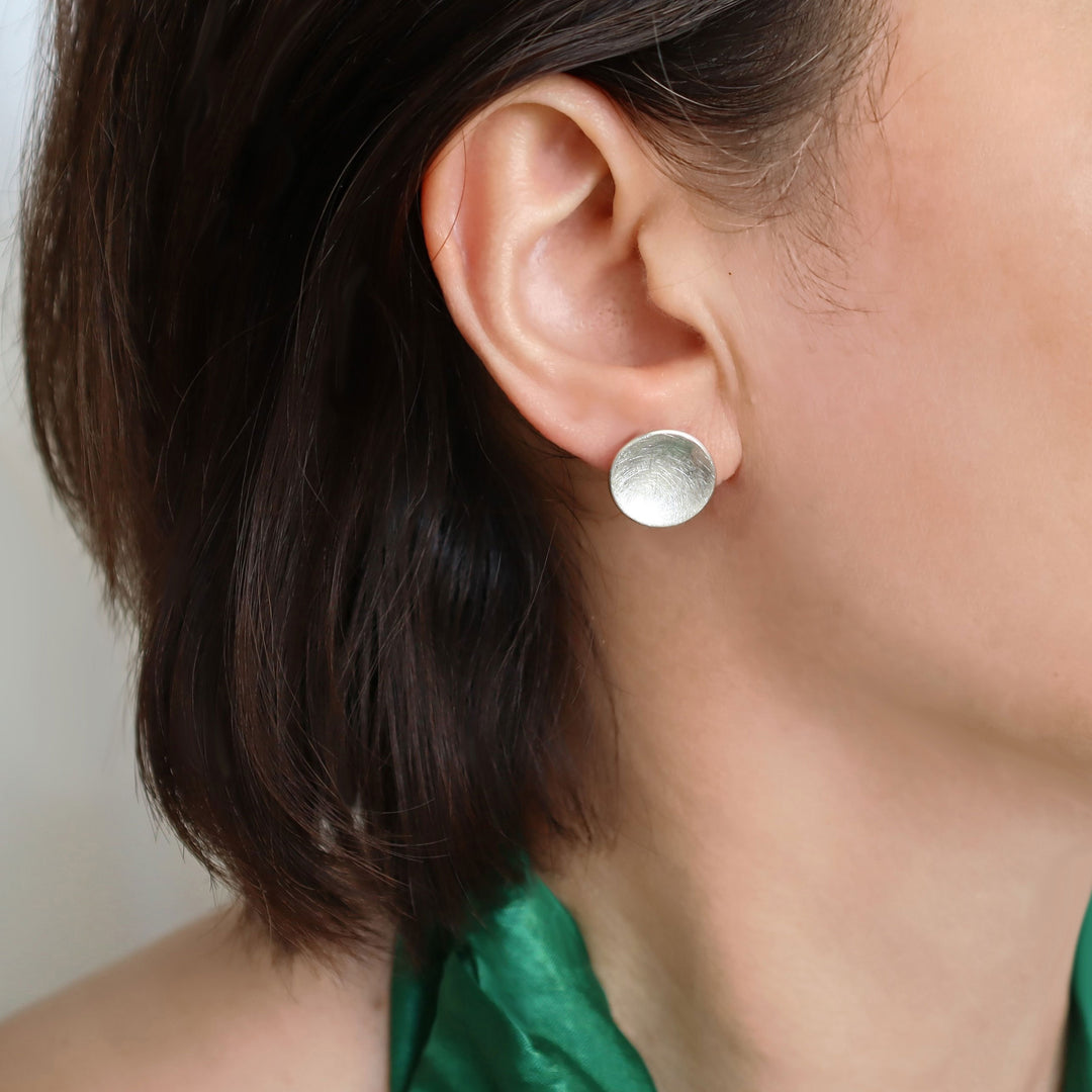 A close-up image of a woman wearing brushed satin sterling silver stud earrings.