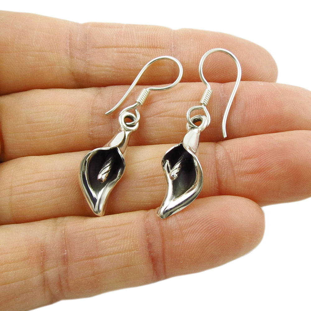 A pair of sterling silver dangling flower earrings designed to resemble a calla lily, held in a hand.