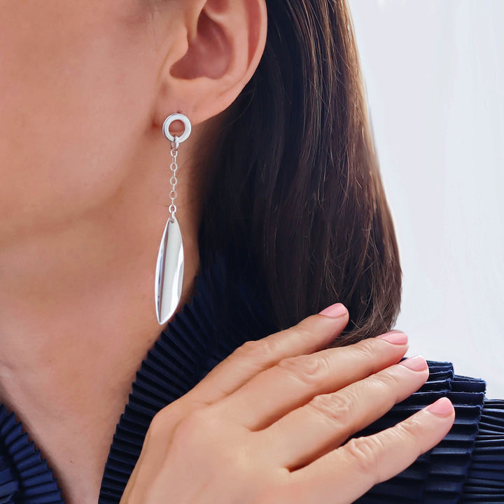 Long sterling silver chain earrings with curved drops worn by a woman with a blue blouse