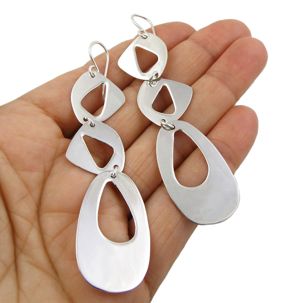 Long asymmetrical 925 silver angled drop earrings held in a person's hand on a white background