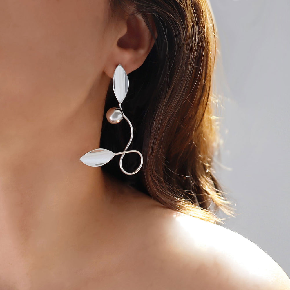 A close-up image of a woman's ear wearing a large silver leaf and berry design earring.
