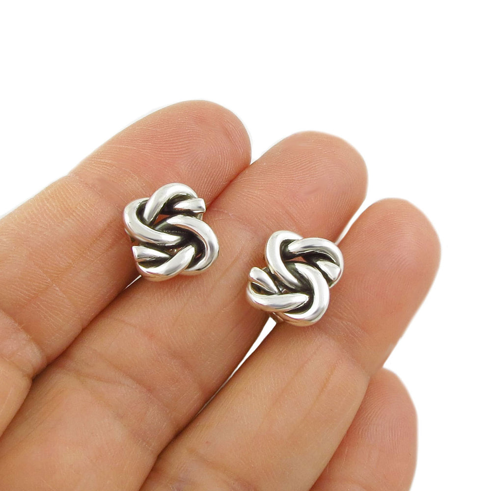 Sterling silver lovers knot stud earrings held between fingers on a white background.
