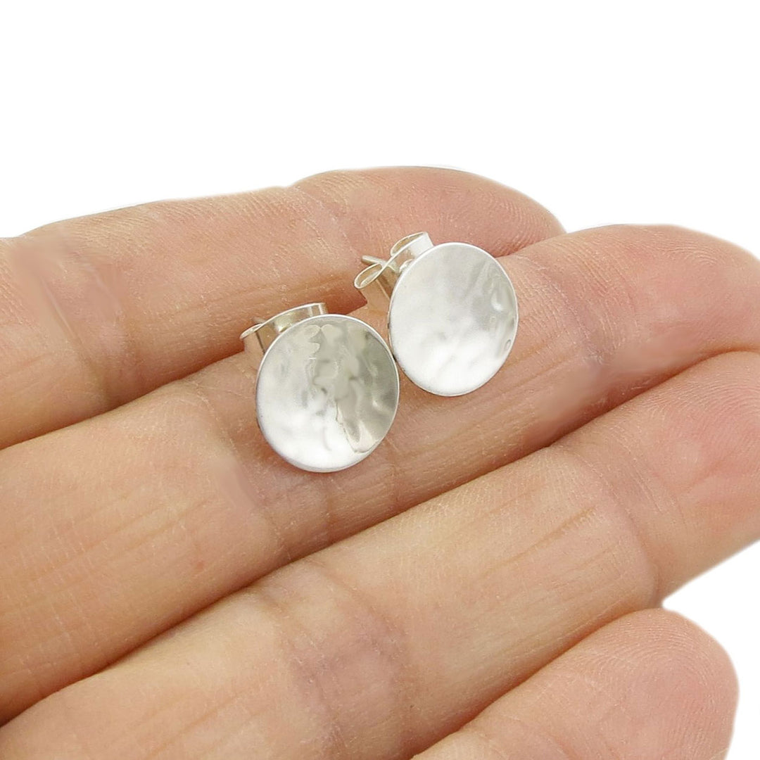 Hammered silver circle stud earrings held in a hand on a white background