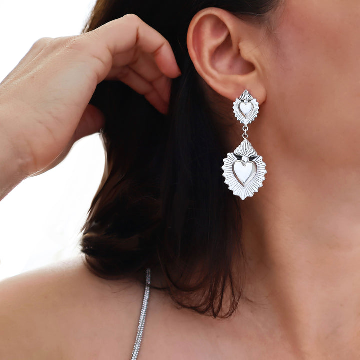 Flaming heart silver earrings being worn by a woman on a white background
