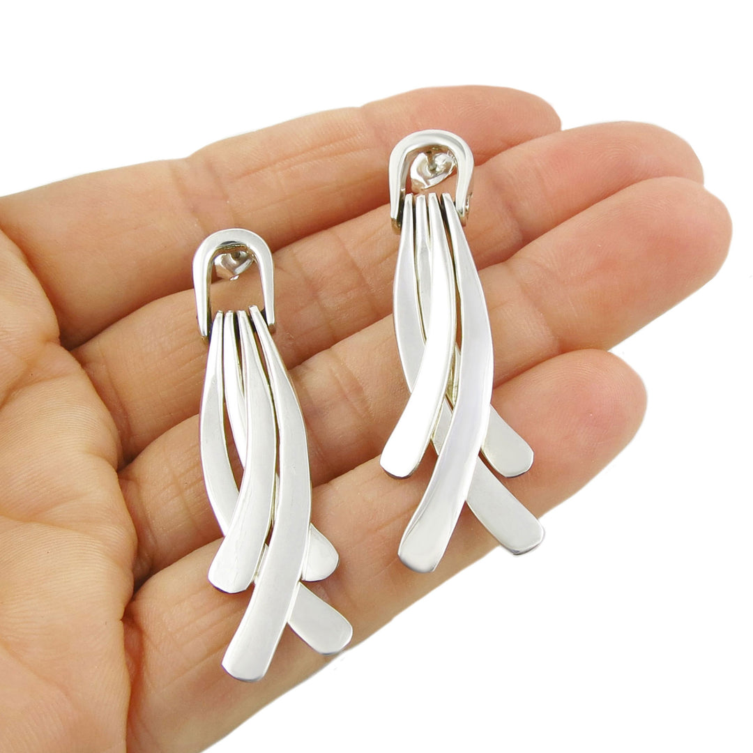 A pair of long sterling silver drop earrings held in a hand, with a polished finish.