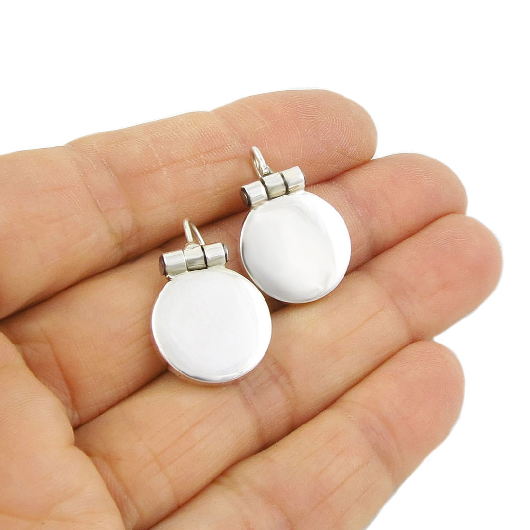 Sterling silver round drop earrings held in a person's hand on a white background.