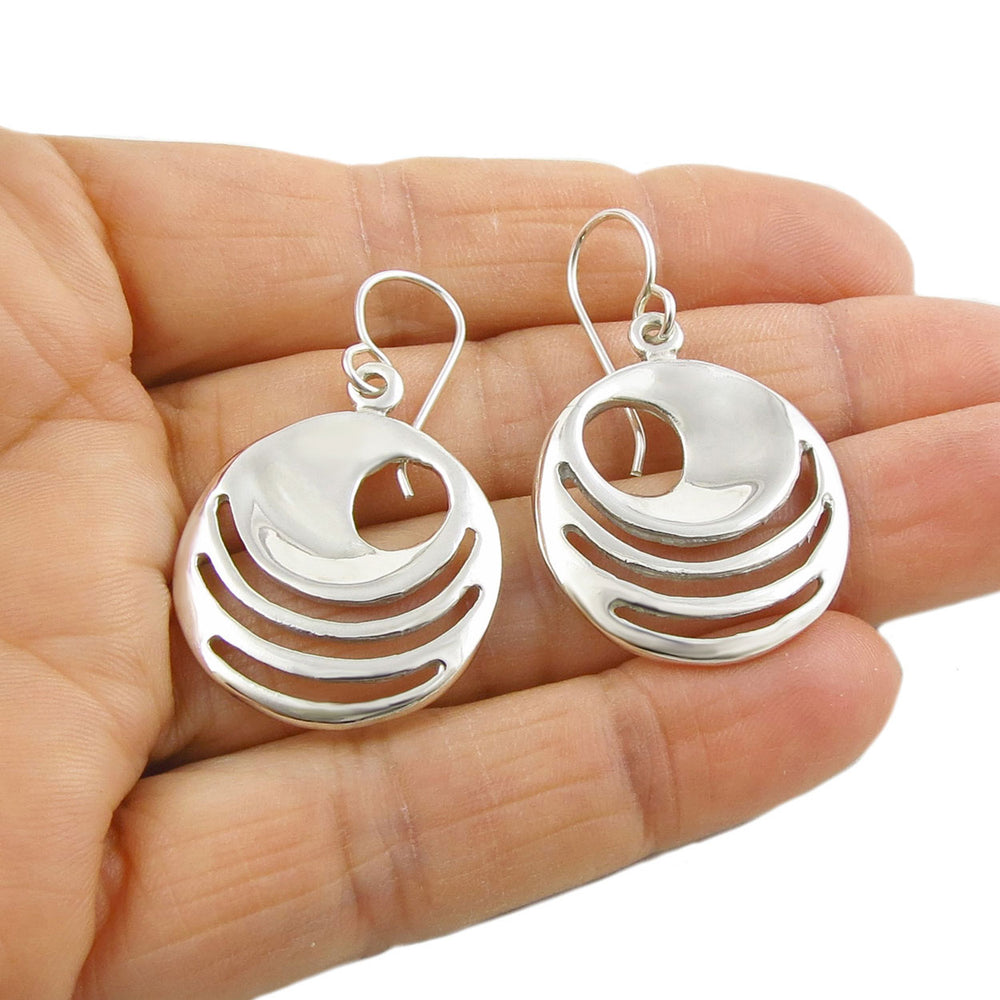 Sterling islver earrings with cut out shapes held in a person's hand