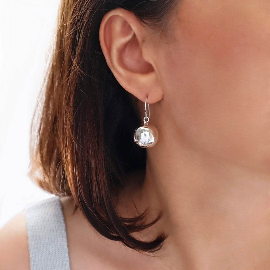 Large hammered silver ball earrings worn by a woman