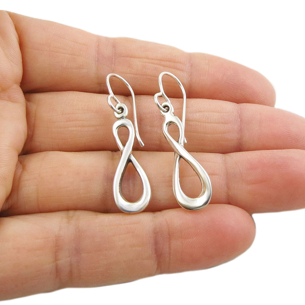 Silver figure of eight earrings held in a person's hand