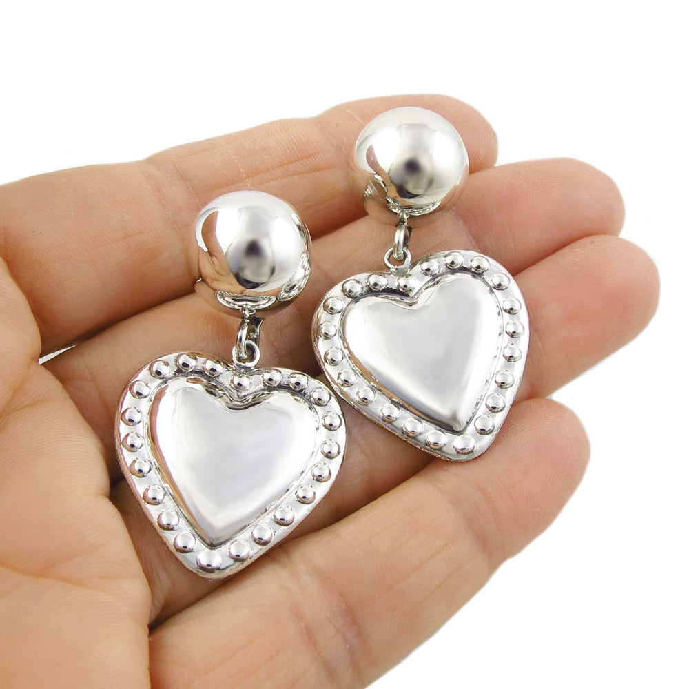 Sterling silver heart earrings held in a person's hand