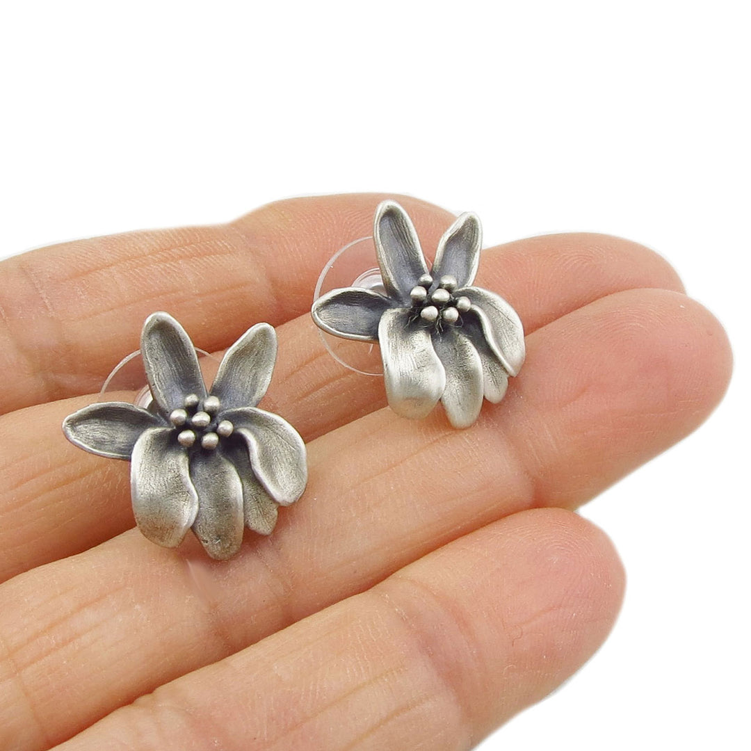 Textured ssolid sterling silver moringa flower stud drop earrings held between fingers.