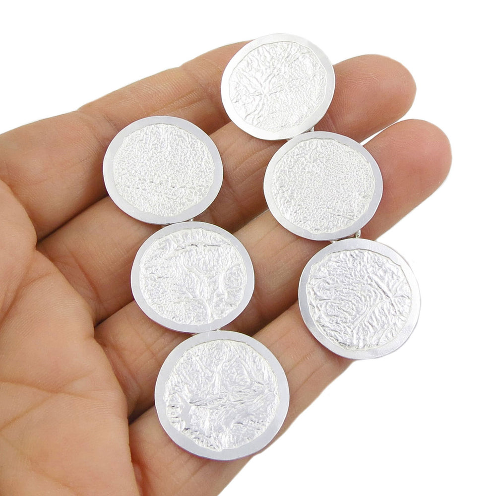 Long triple circle drop sterling silver earroings with a crumpled finish held in  a person's hand.