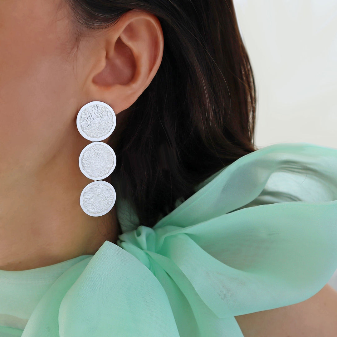 Long triple circle drop earrings in sterling silver with a crumpled reticulated finish worn vby a woman with a green blouse.