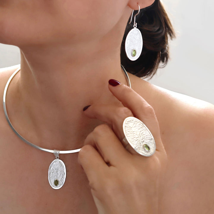 Matching peridot gemstone earrings, ring and pendant worn by a woman with a silver choker necklace