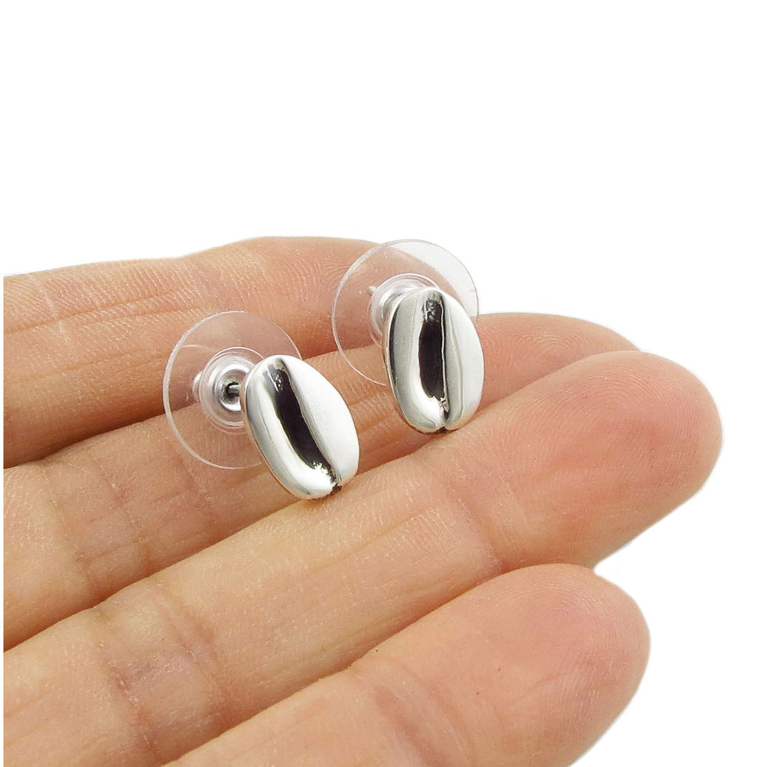 A pair of silver stud earrings designed to resemble coffee beans, held in a person's hand.