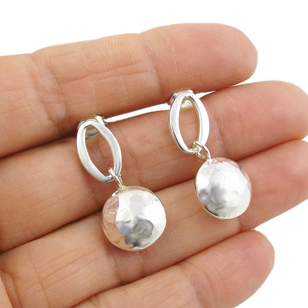 Silver drop earrings with a hammered finish being held in a person's hand