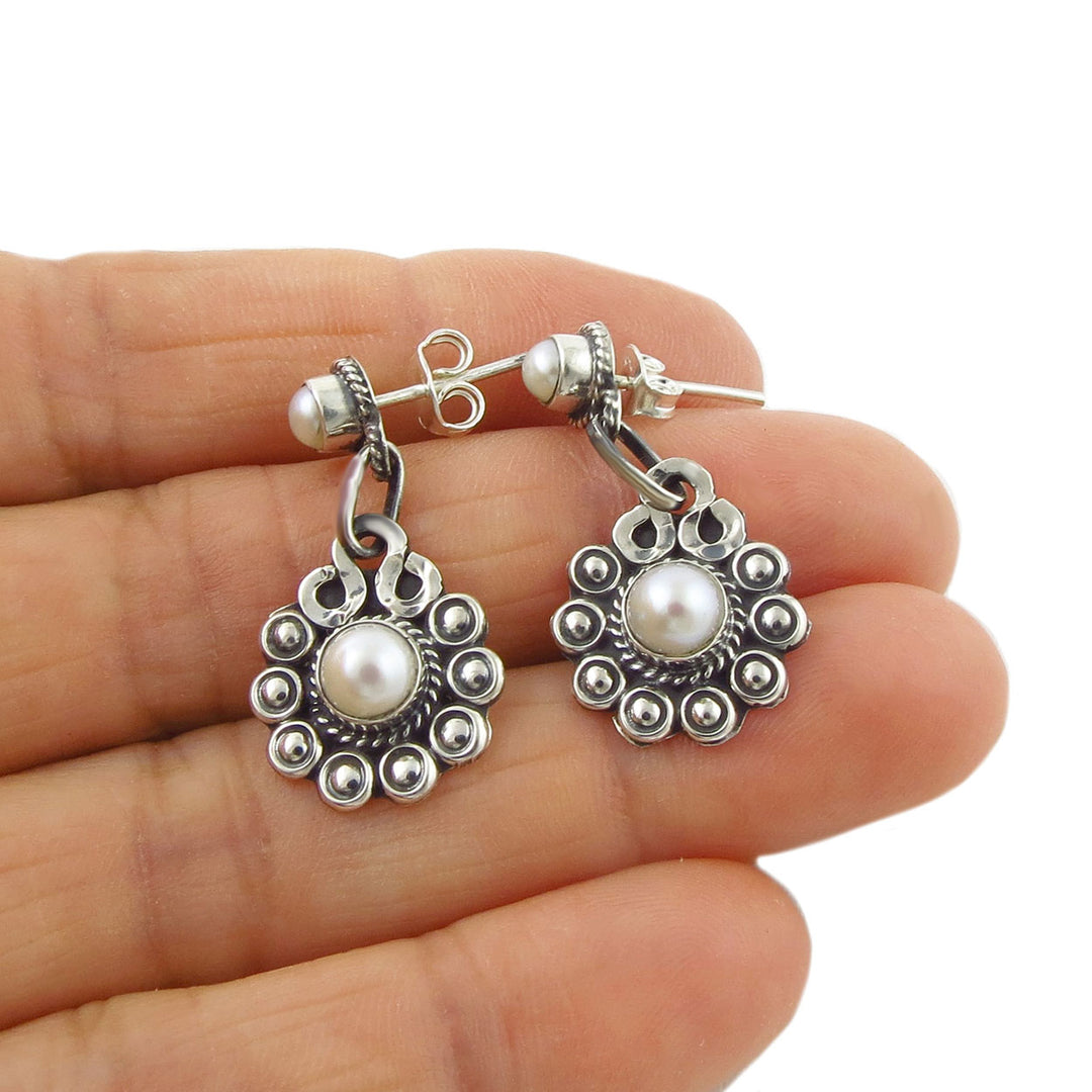 Sterling silver daisy flower earrings with faux pearls held in a person's hand on a white backgroubd.
