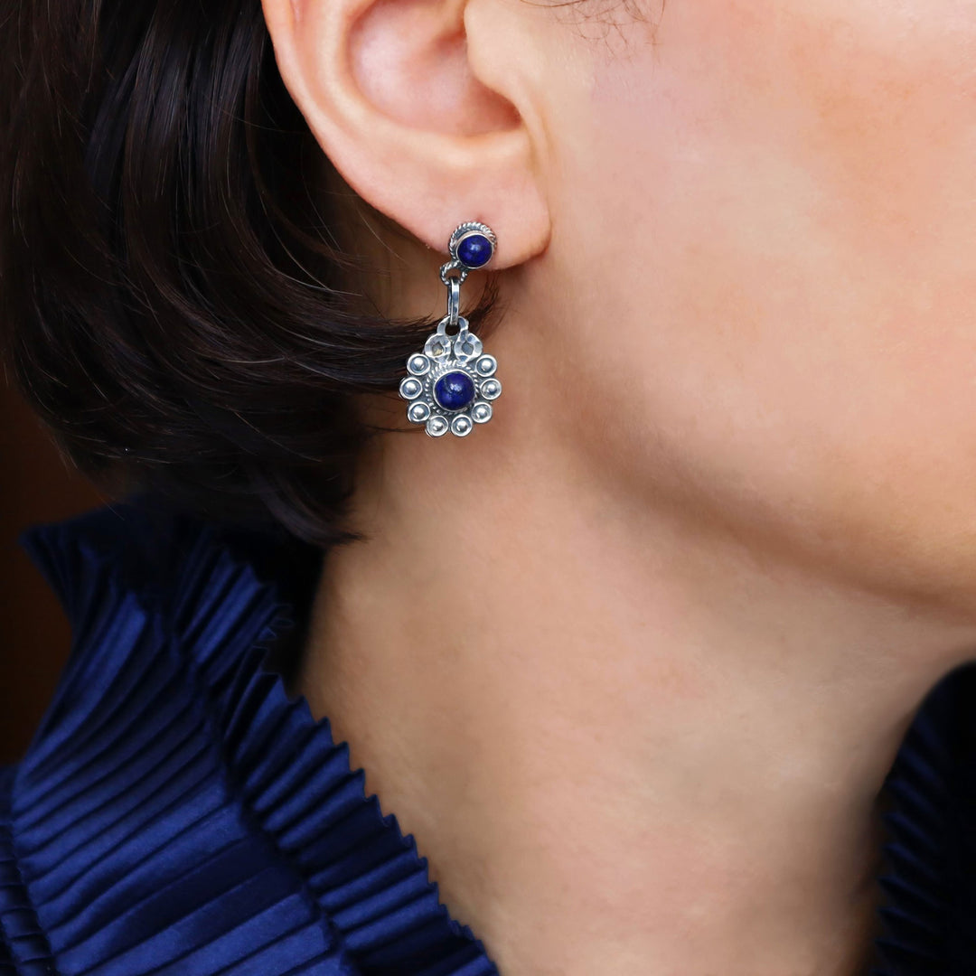 Daisy flower earrings in 925 silver with lapis lazuli gemstones worn by a woman with a blue blouse.