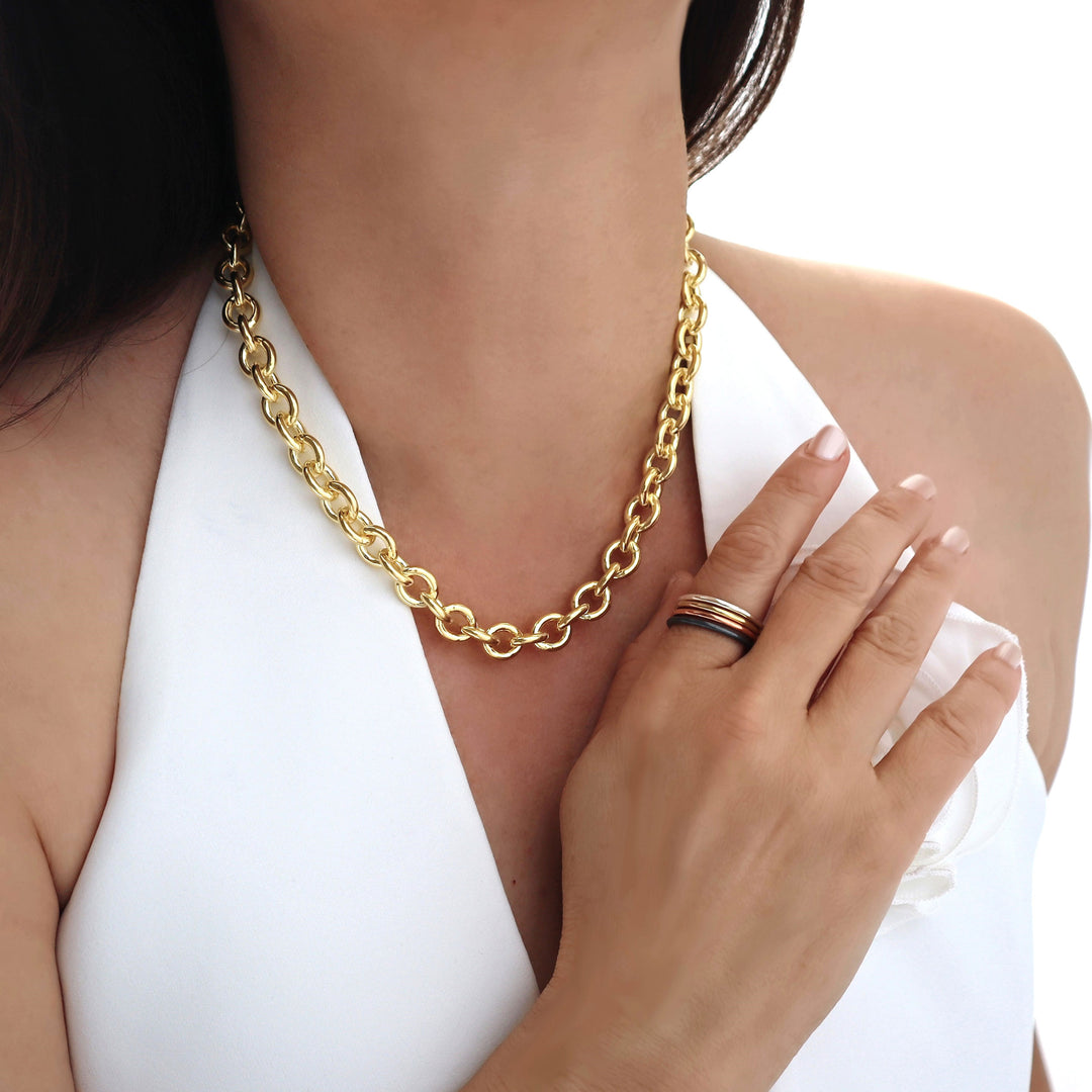 Yellow gold chain necklace and ring stack worn by a woman with a white waistcoat