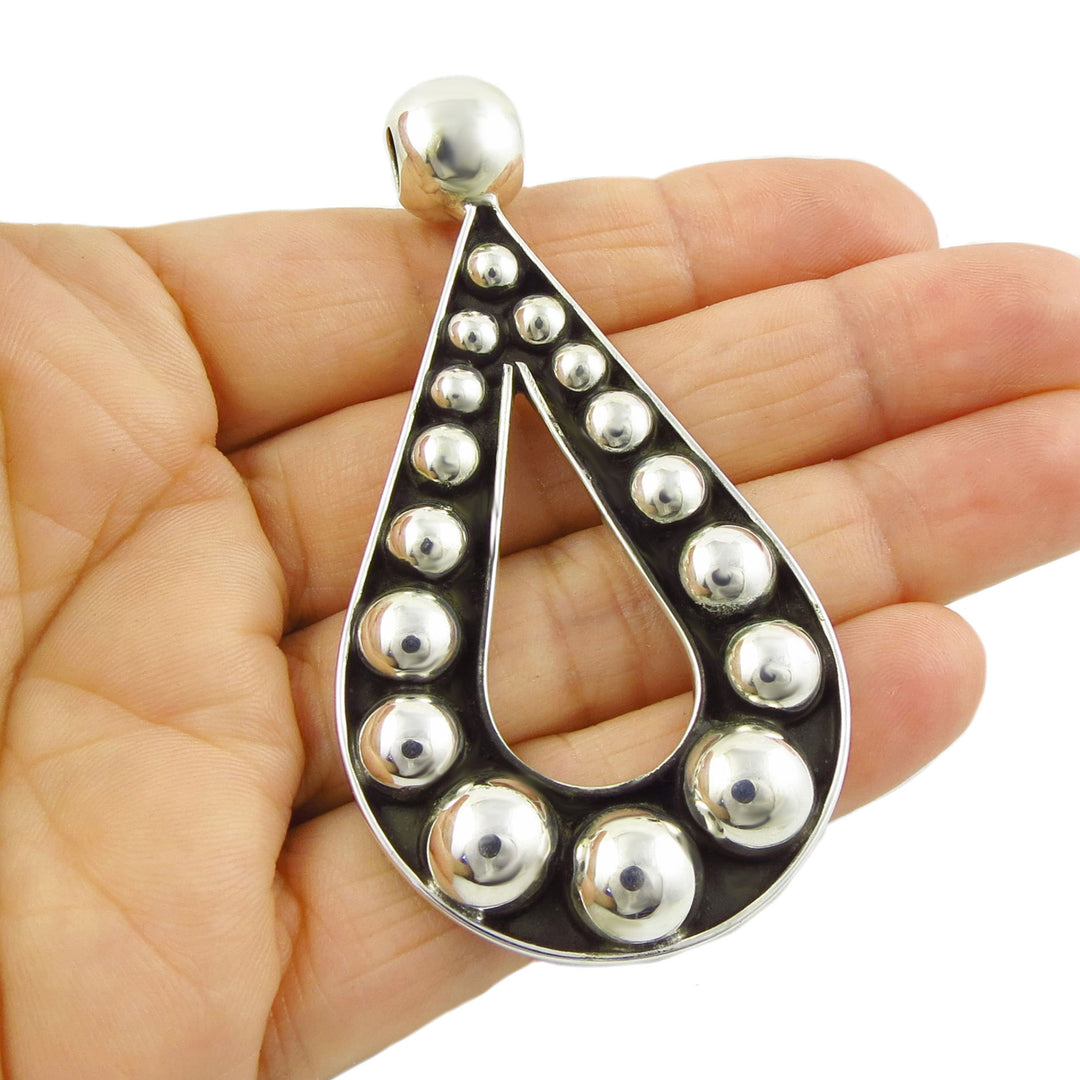 A large sterling silver pendant with a blackened base and polished beafds held in a person's hand on a white background.