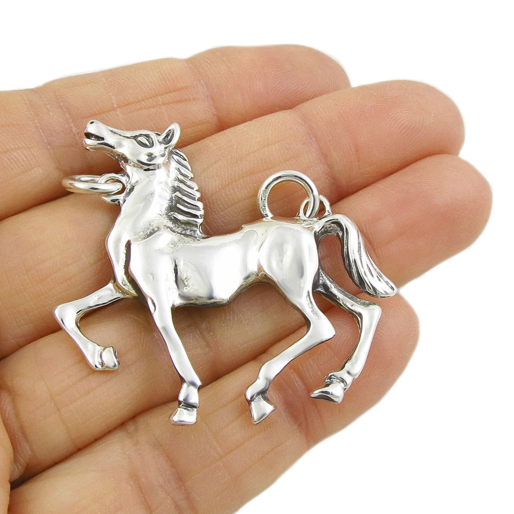 A large sterling silver horse shaped pendant held in a person's hand.