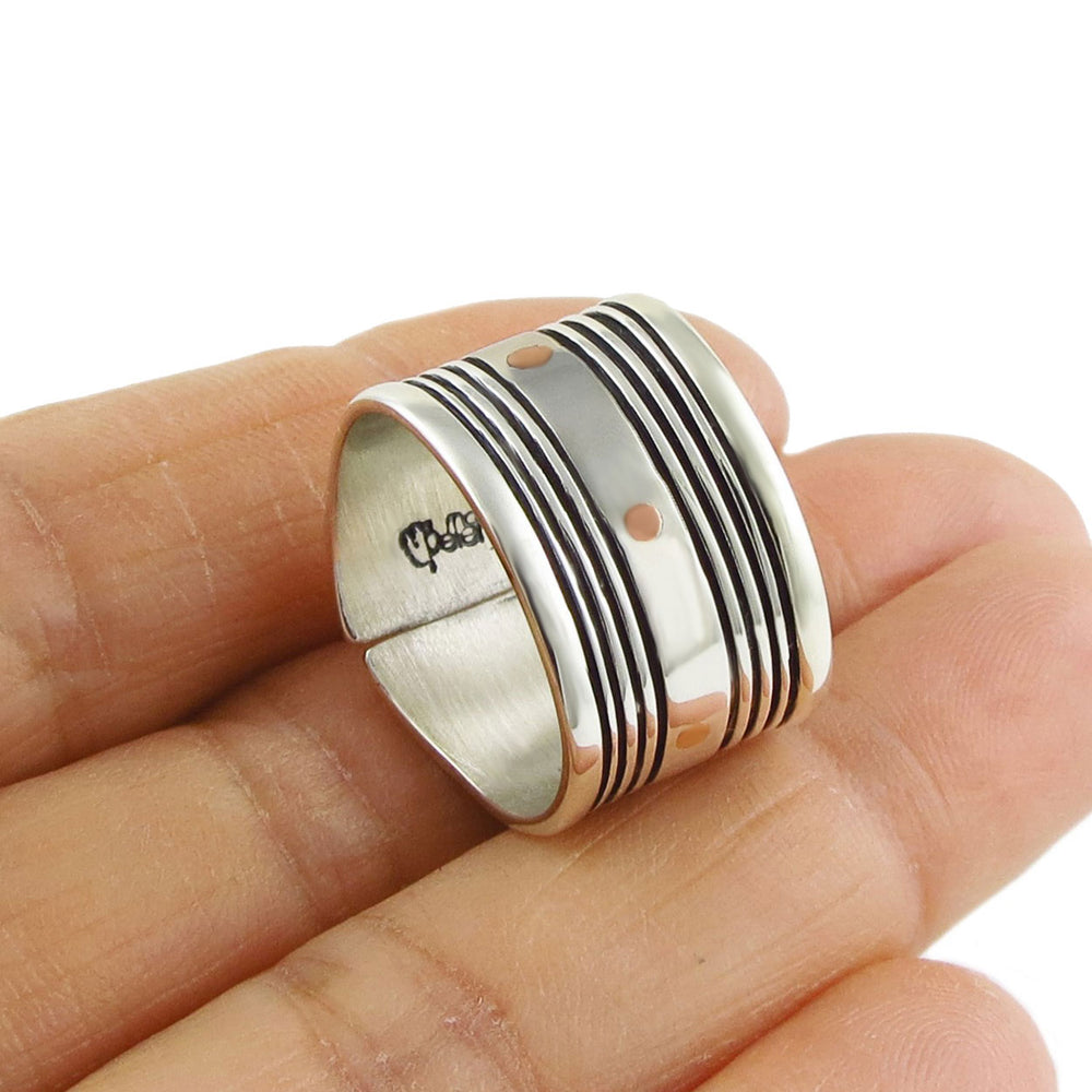 A wide sterling silver band ring with copper accents being held in a hand on a white background.