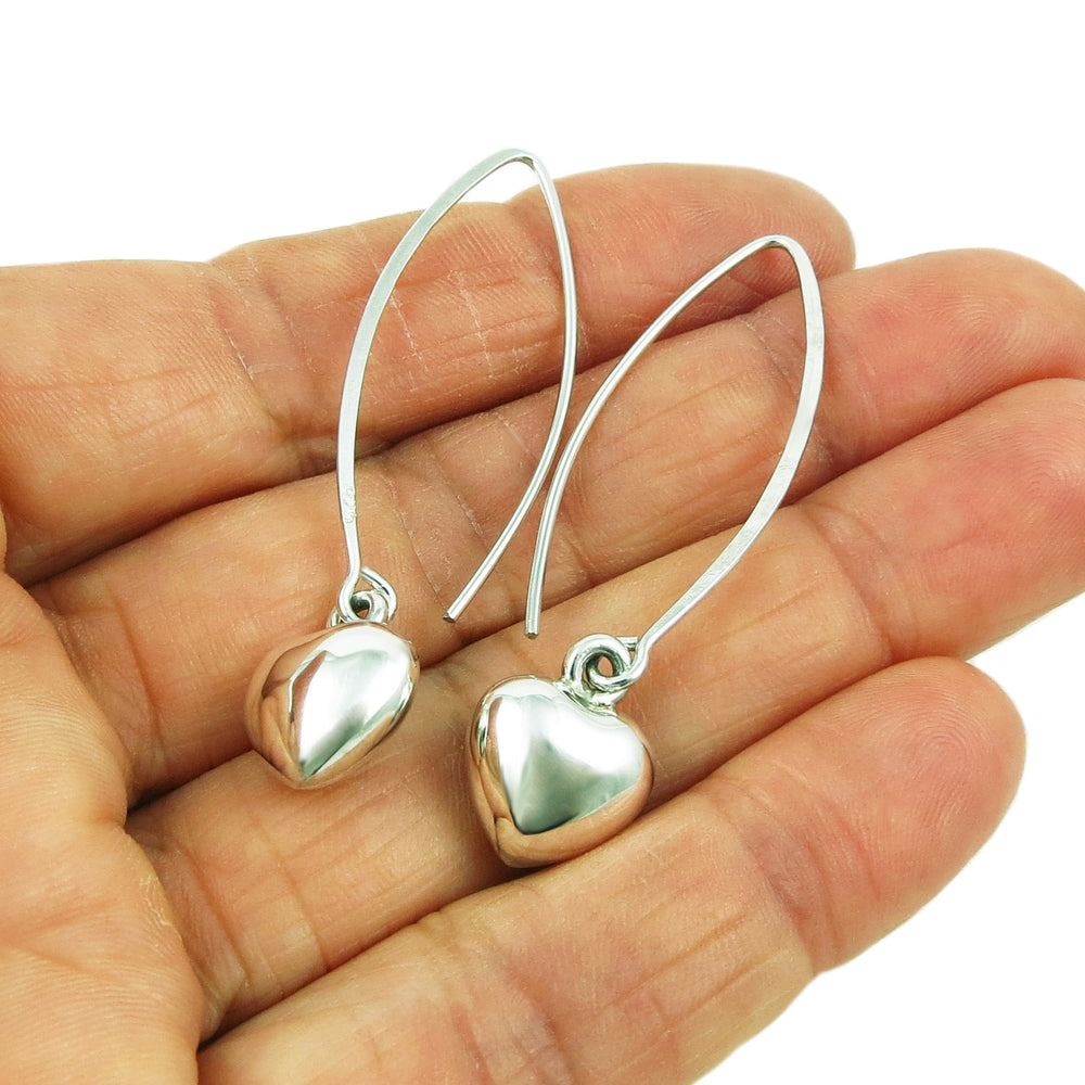 Long silver threader earrings with dangling puffed hearts held in a person's hand on a white background