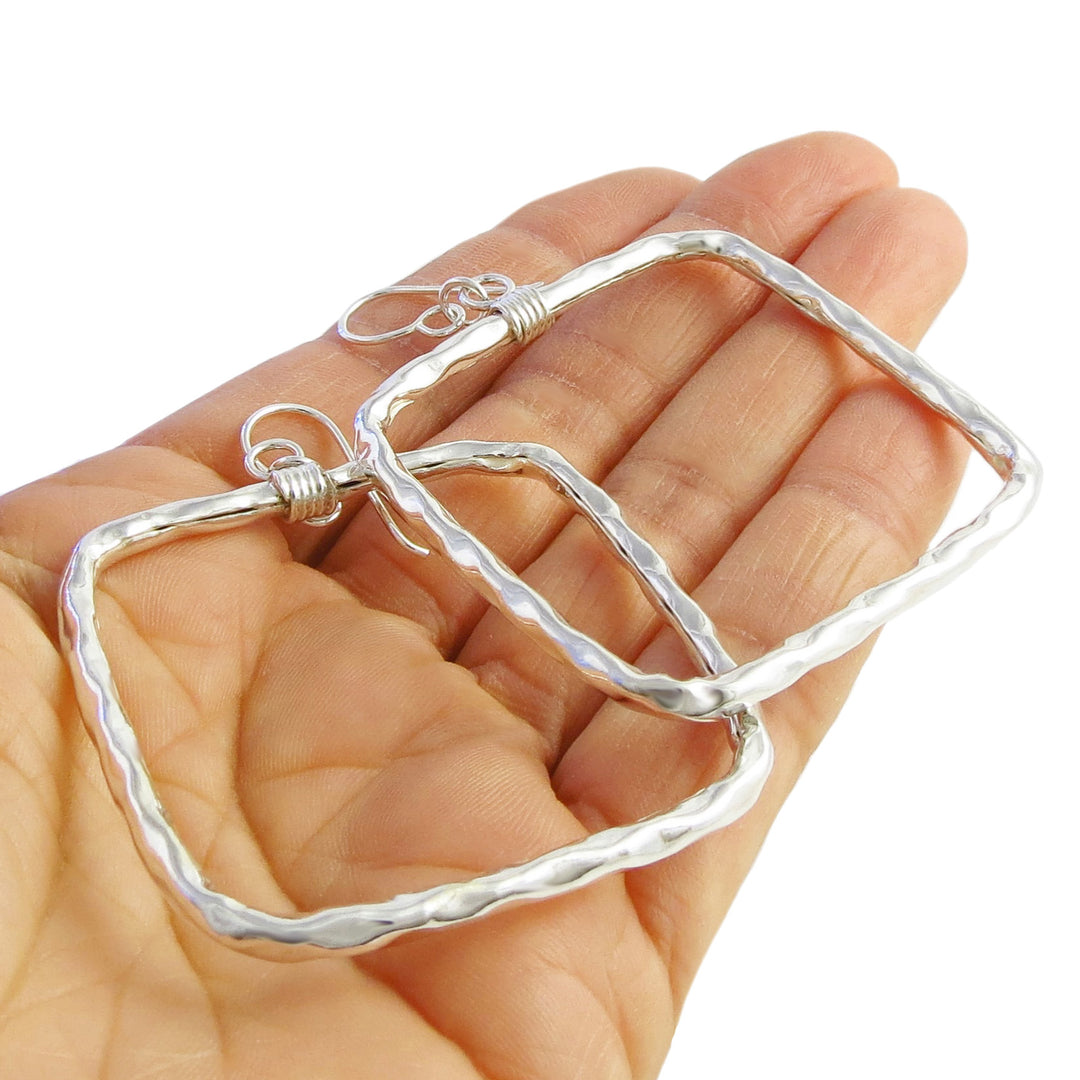 Hammered 925 silver square hoop earrings held in a person's hand on a white background