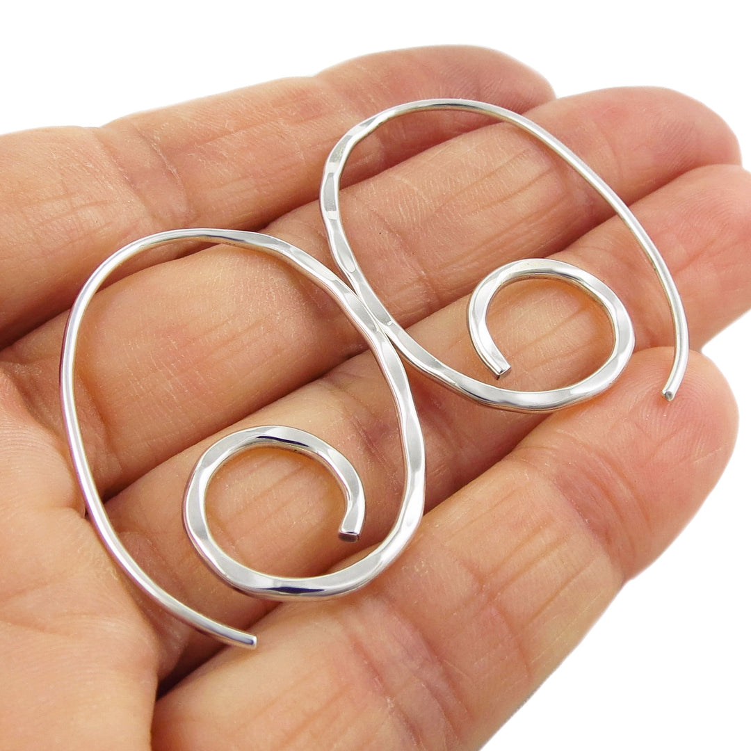 A pair of silver spiral threader earrings with a hammered finish displayed on a hand.