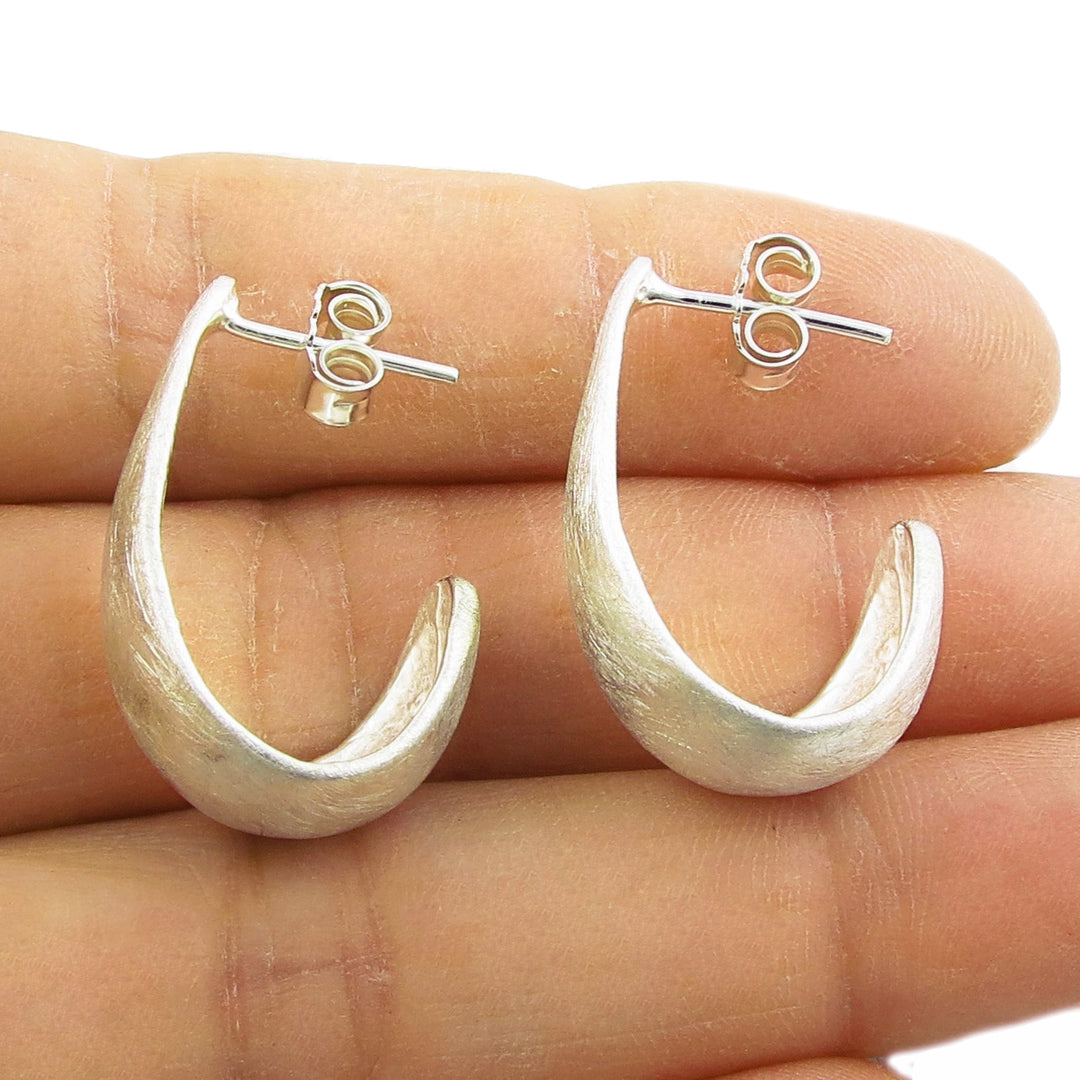 A pair of silver hoop earrings resting on a person's hand.