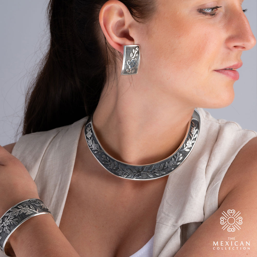 A woman wearing sterling silver earrings with a floral design, paired with a matching bracelet and necklace.