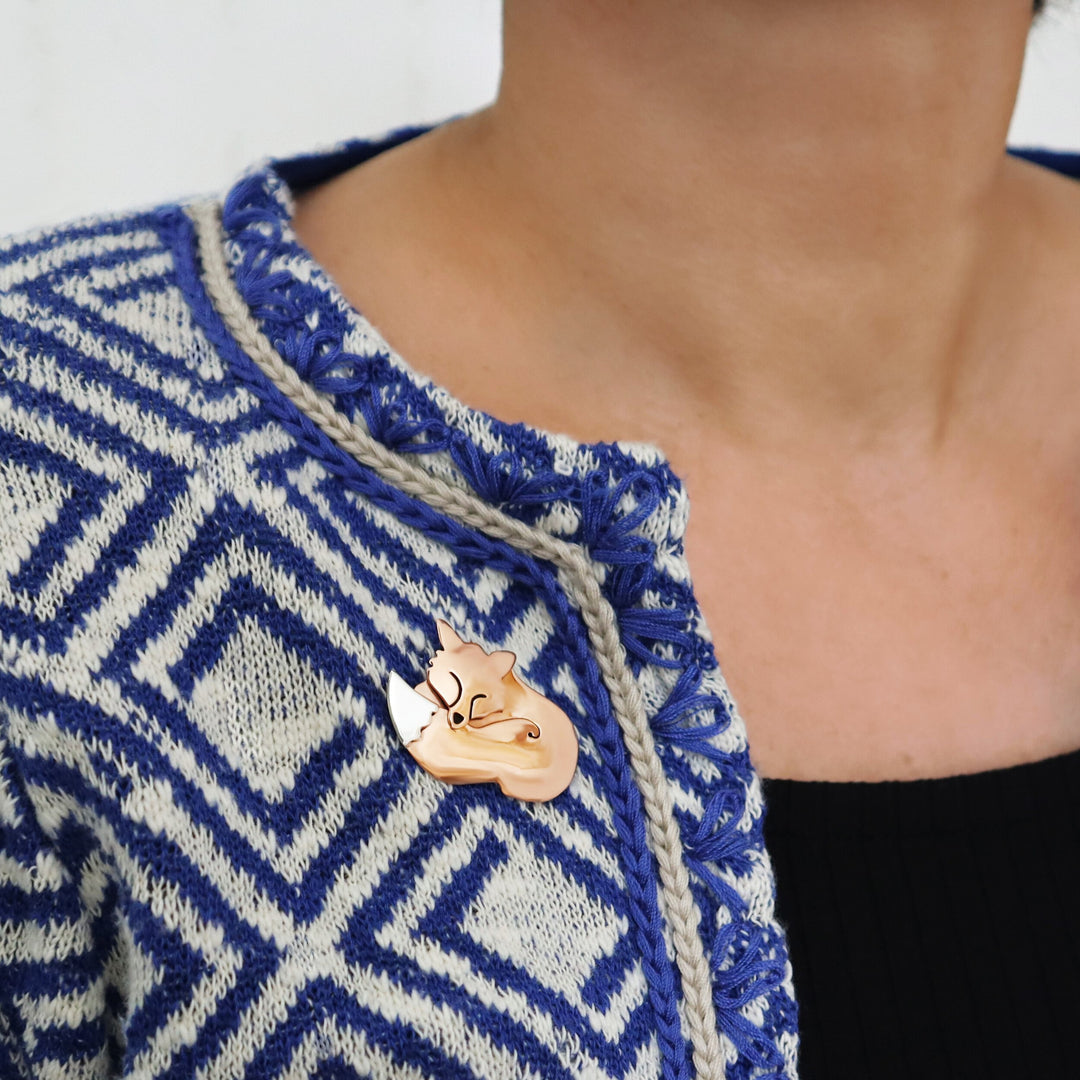 A woman wearing  ablue and white coat with a copper and ssilver fox brooch.