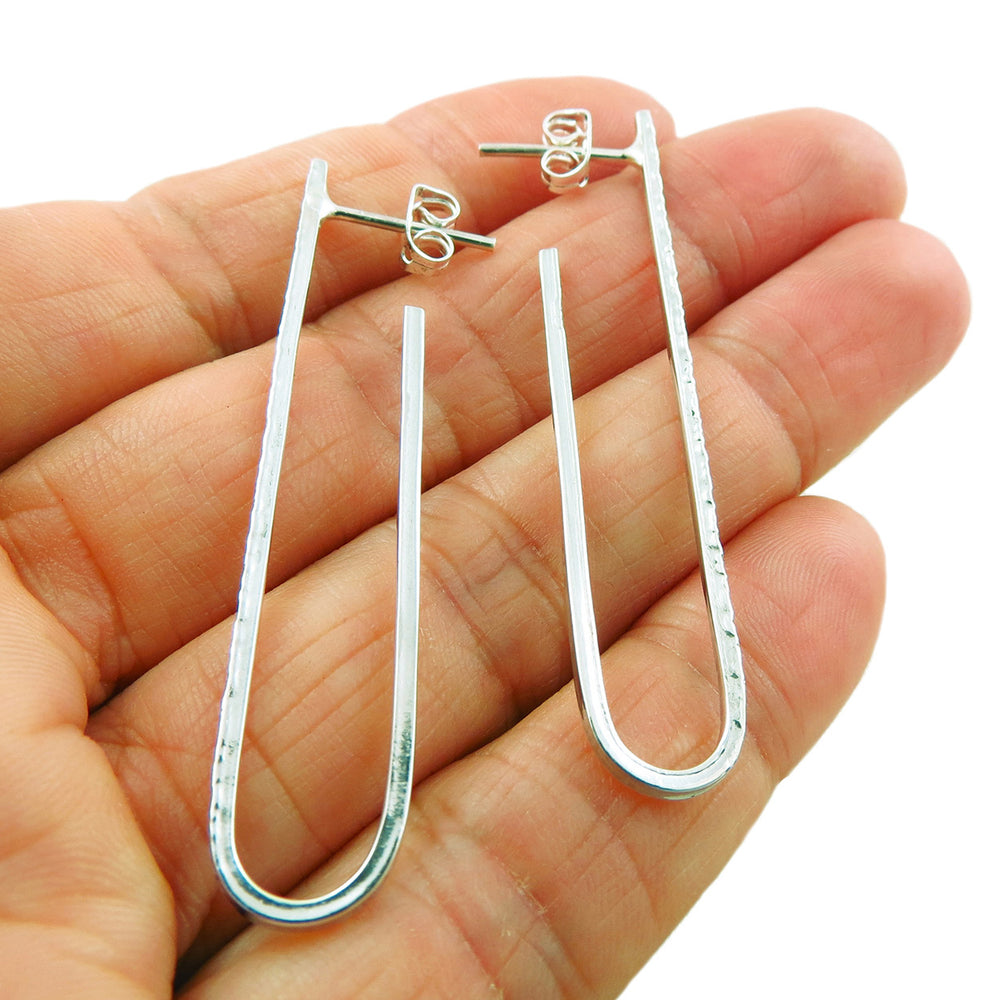 A pair of long u-shaped silver earrings held in a person's hand