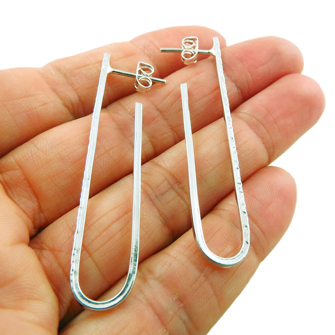 A pair of long u-shaped silver earrings held in a person's hand