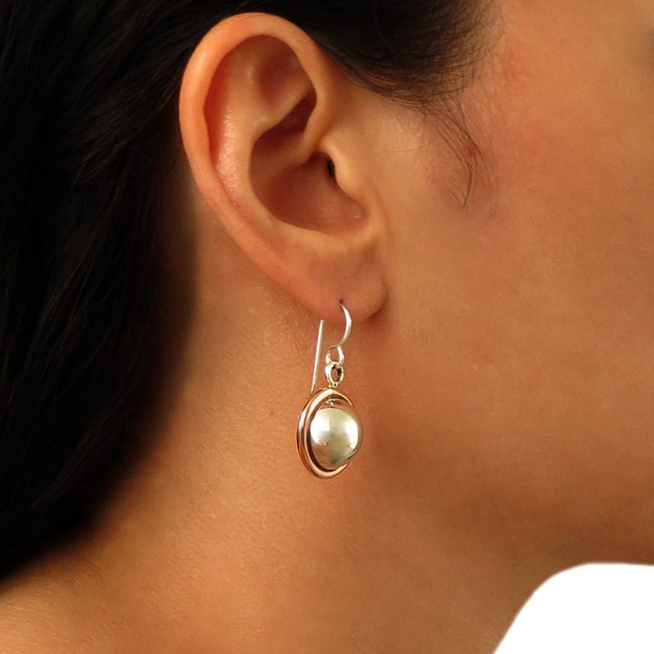 Silver earrings with a copper border worn by a person with dark hair.