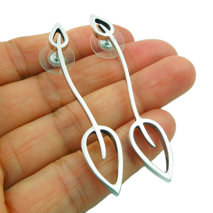 A pair of sterling silver leaf earrings held in a person's hand on a white background