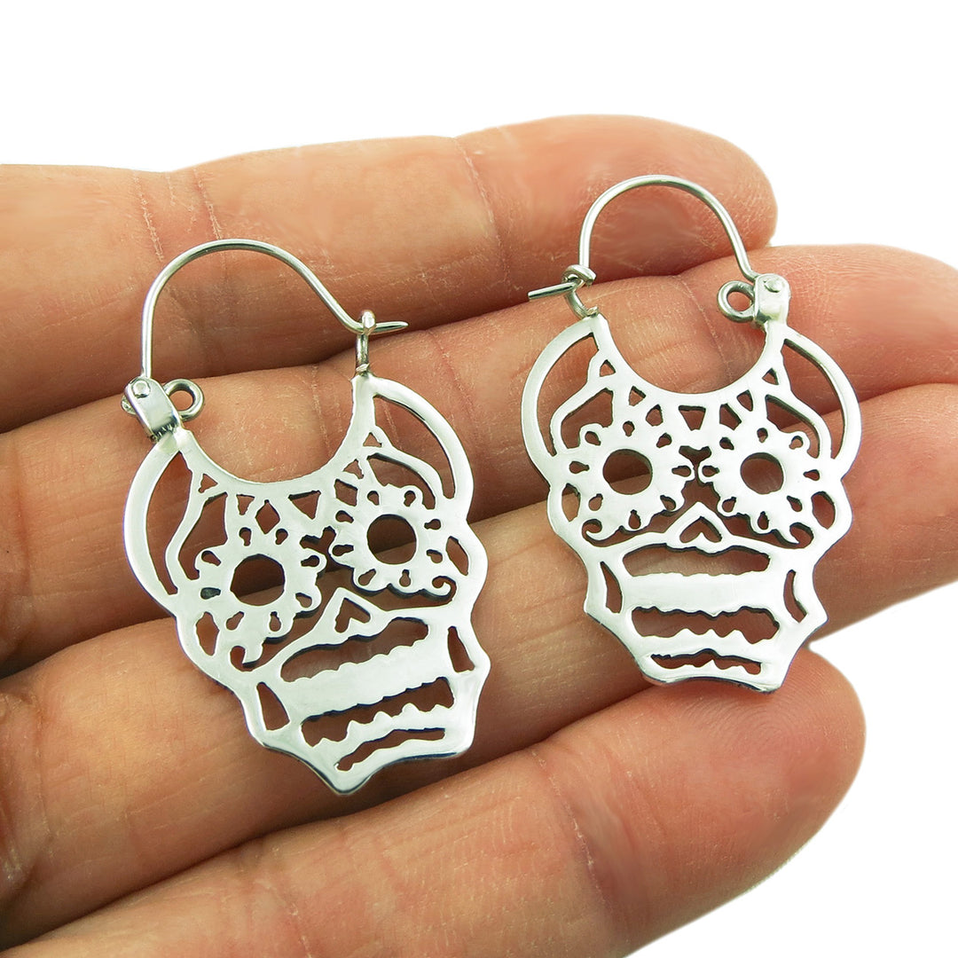 Day of the dead silver ugar skull earrings held in a person's hand.
