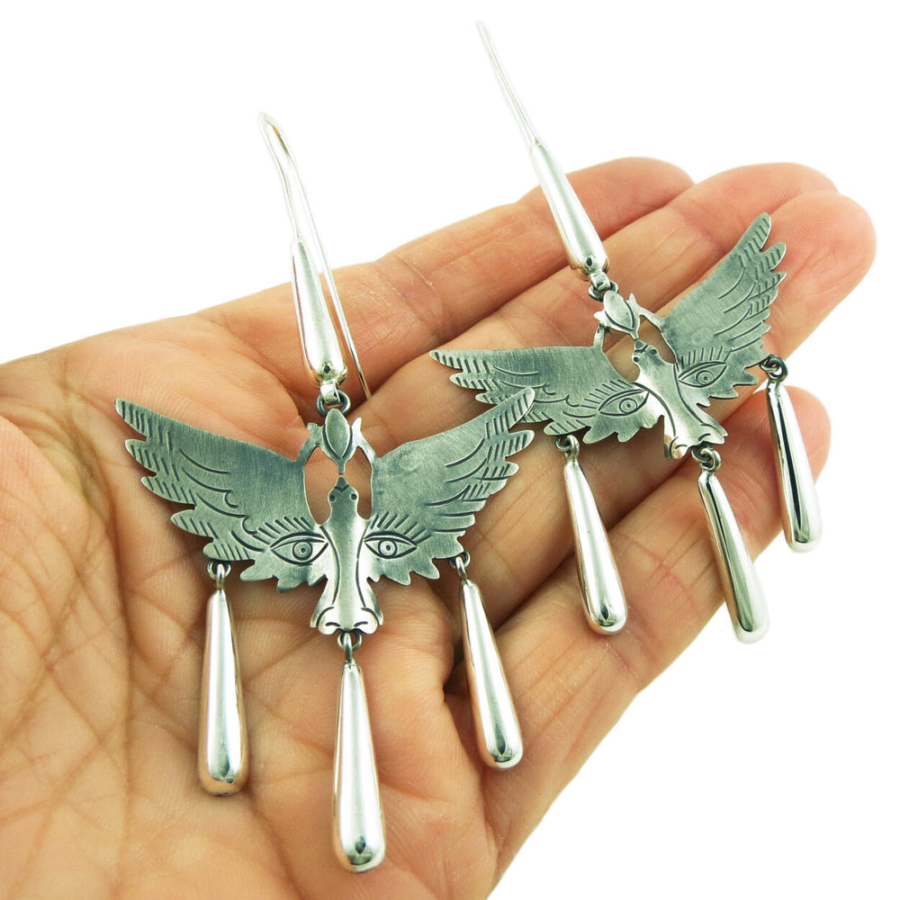 Winged Mexican folklore earrings held in a person's hand on a white background.