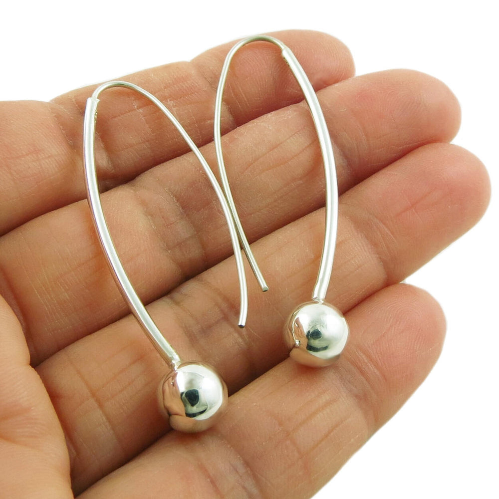 A pair of silver threader drop earrings with ball beads, held in a person's hand.