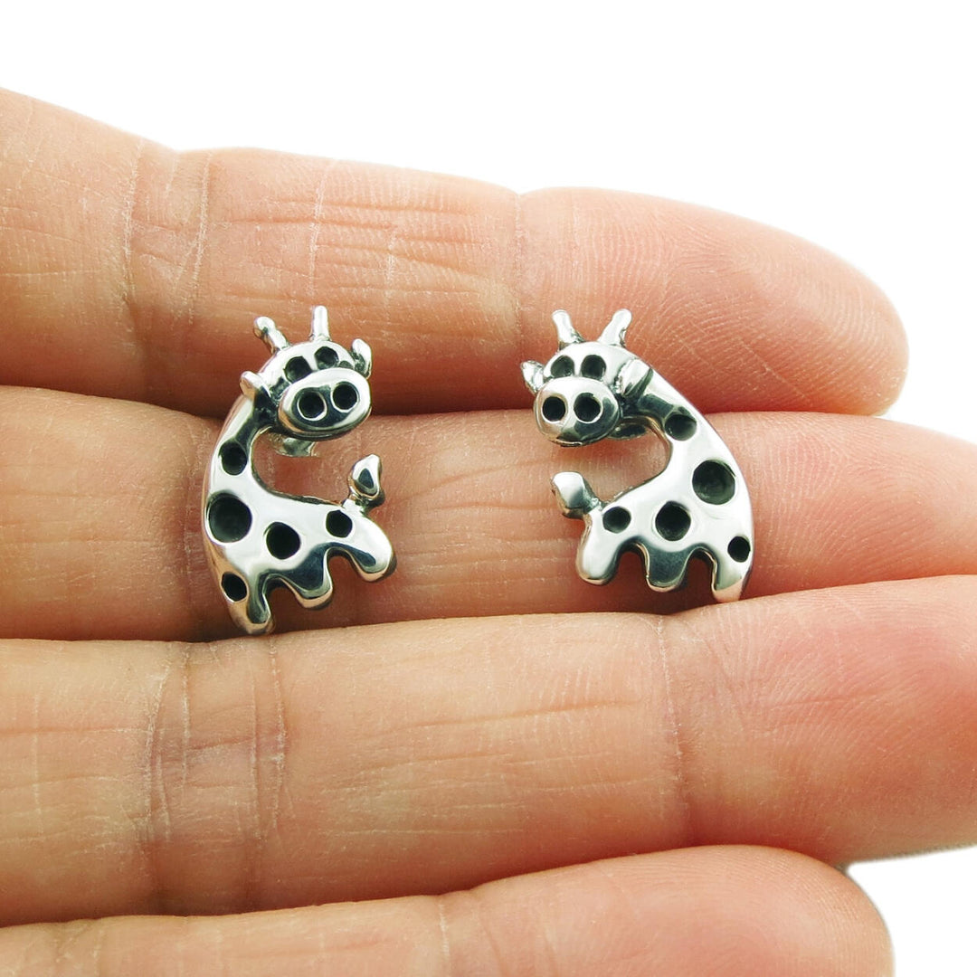Silver giraffe earrings held in a person's hand