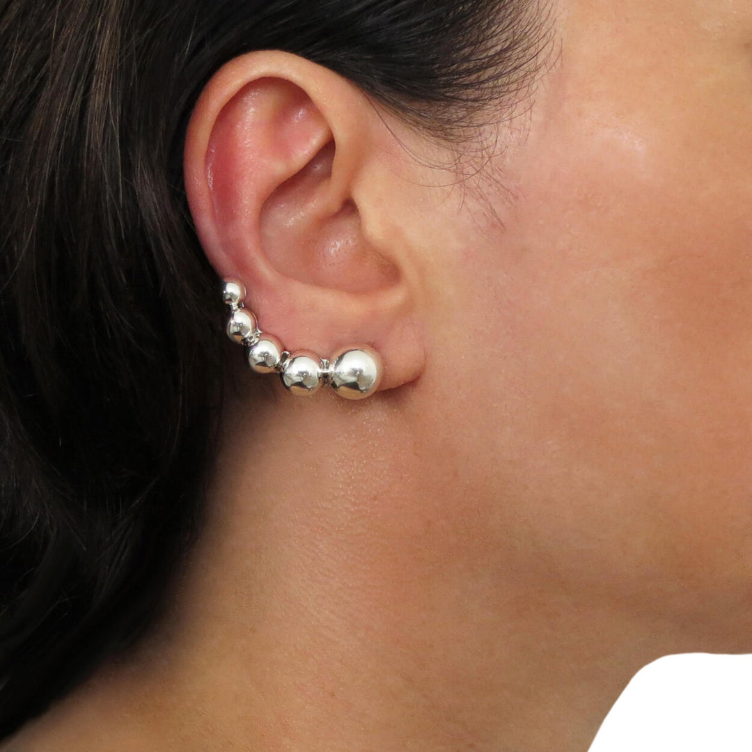 A person wearing a silver ear climber cuff earring with a row of gradiating demi beads.