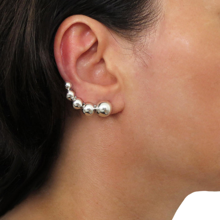 A person wearing a silver ear climber cuff earring with a row of gradiating demi beads.