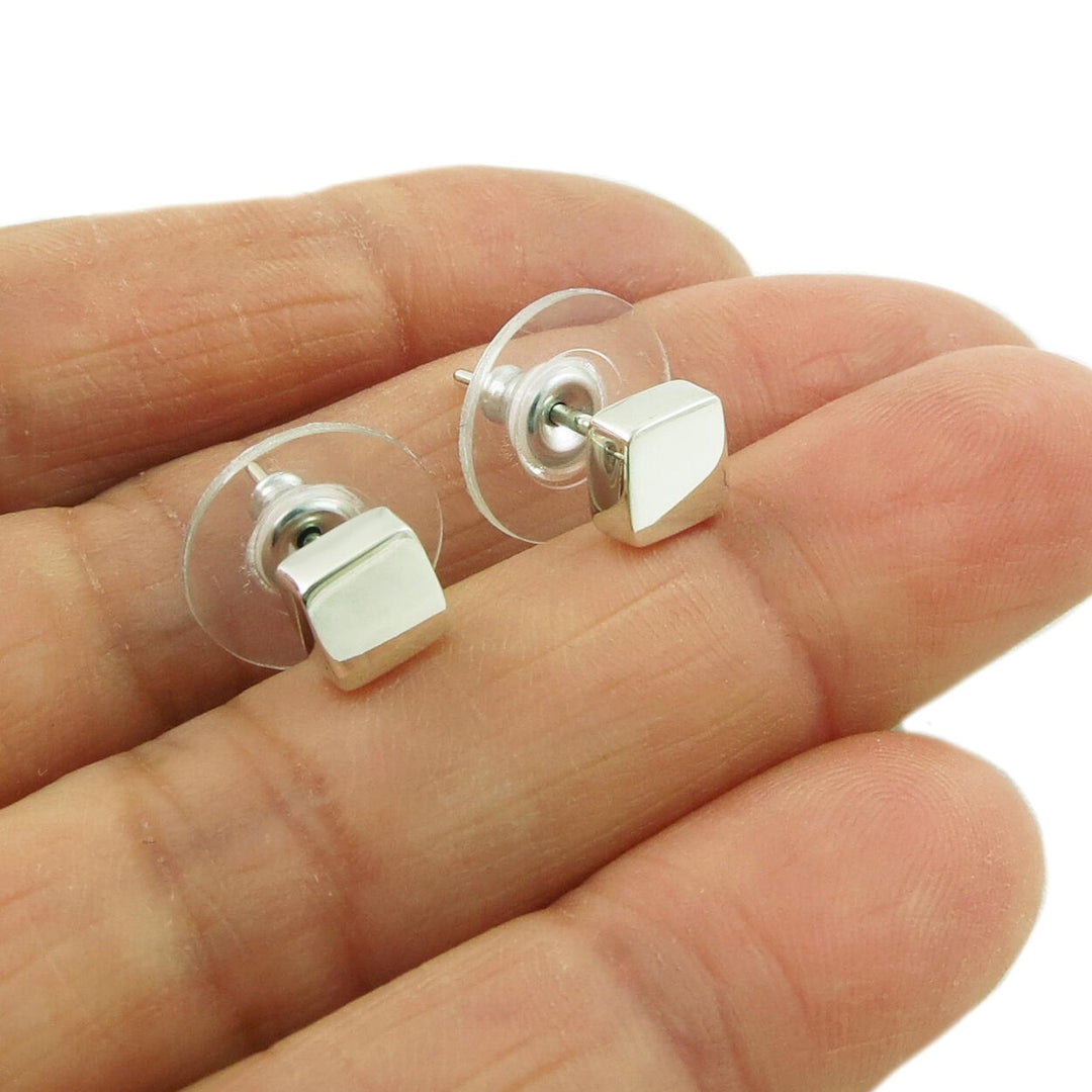 A pair of polished cube stud earrings made of solid 925 sterling silver, held in a person's hand.