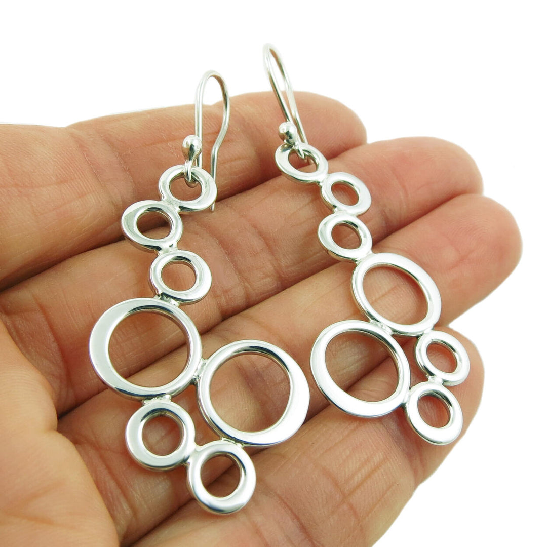 A pair of sterling silver bubble design earrings held in a person's hand.