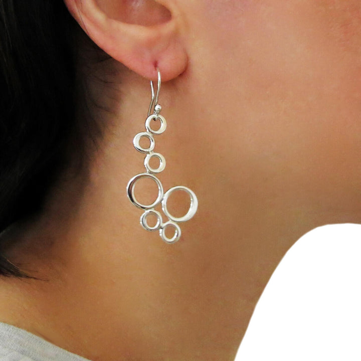 Silver bubble drop earrings worn by a person on a white background