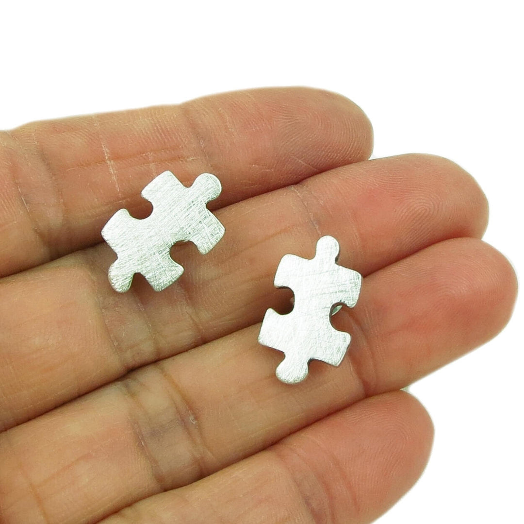 Silver earrings in the shape of jigsaw pieces held in a person's hand on a white background