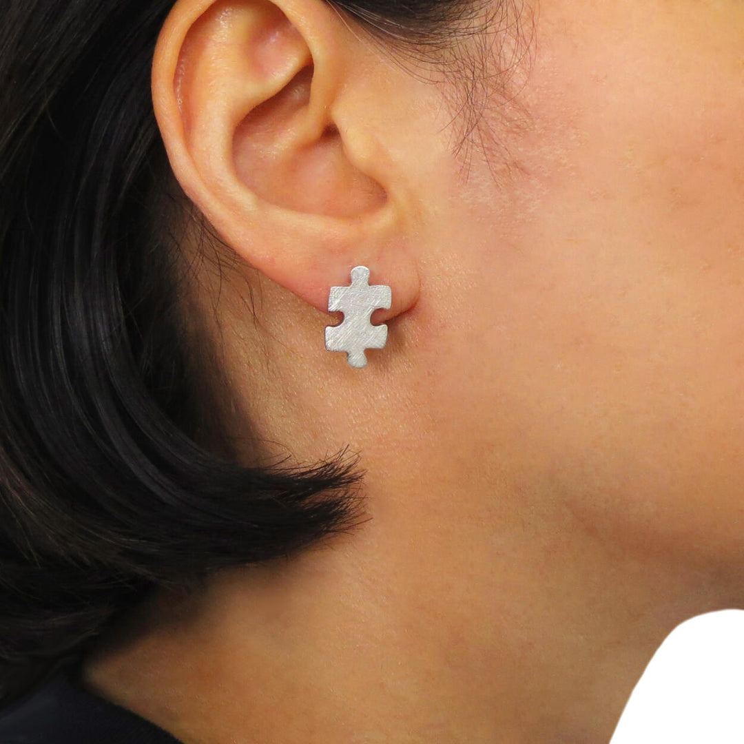 A woman wearing a silver earring in the shape of jigsaw piece on a white background
