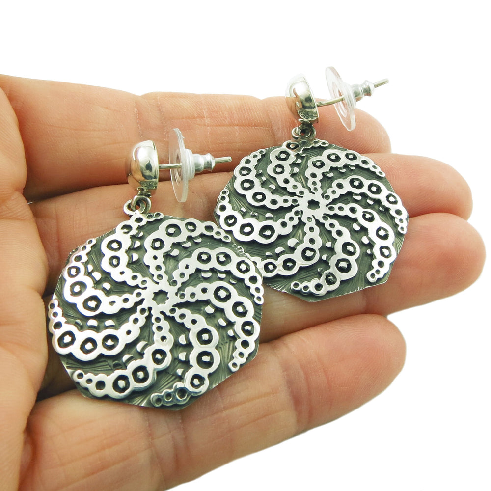 Maria Belen Nilson sterling silver earrings with a spiral pattern held in a person's hand.
